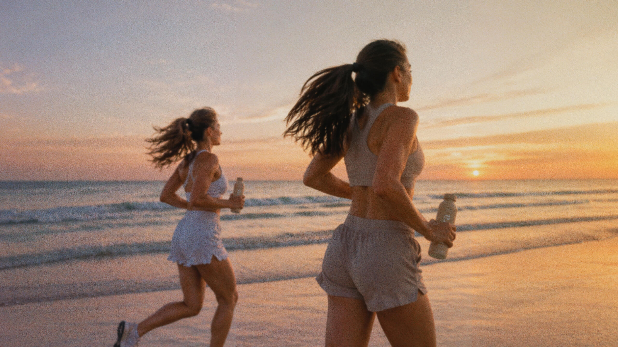 Two women running along the beach at sunset while carrying Lyra bottles